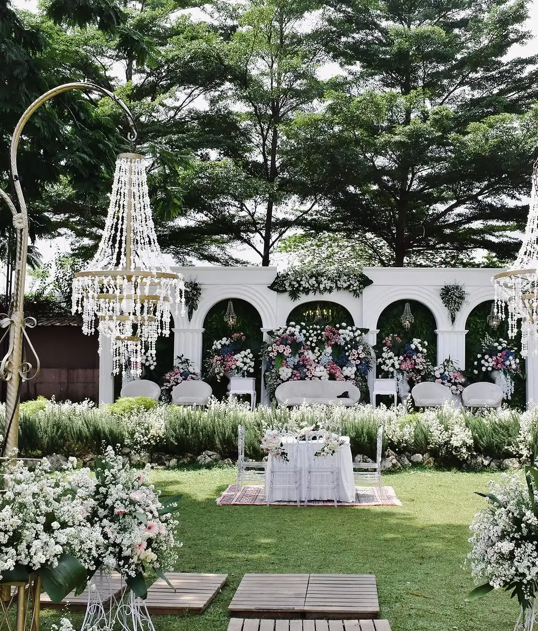 Dekorasi wedding dengan lampu kristal dan gerbang putih di atas rumput