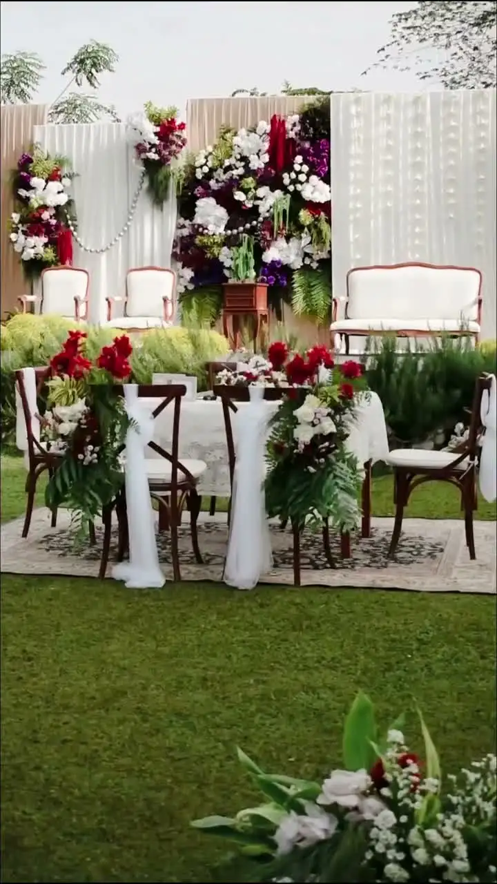 Pelaminan draperi putih dan hijau sage berhias bunga di atas rumput