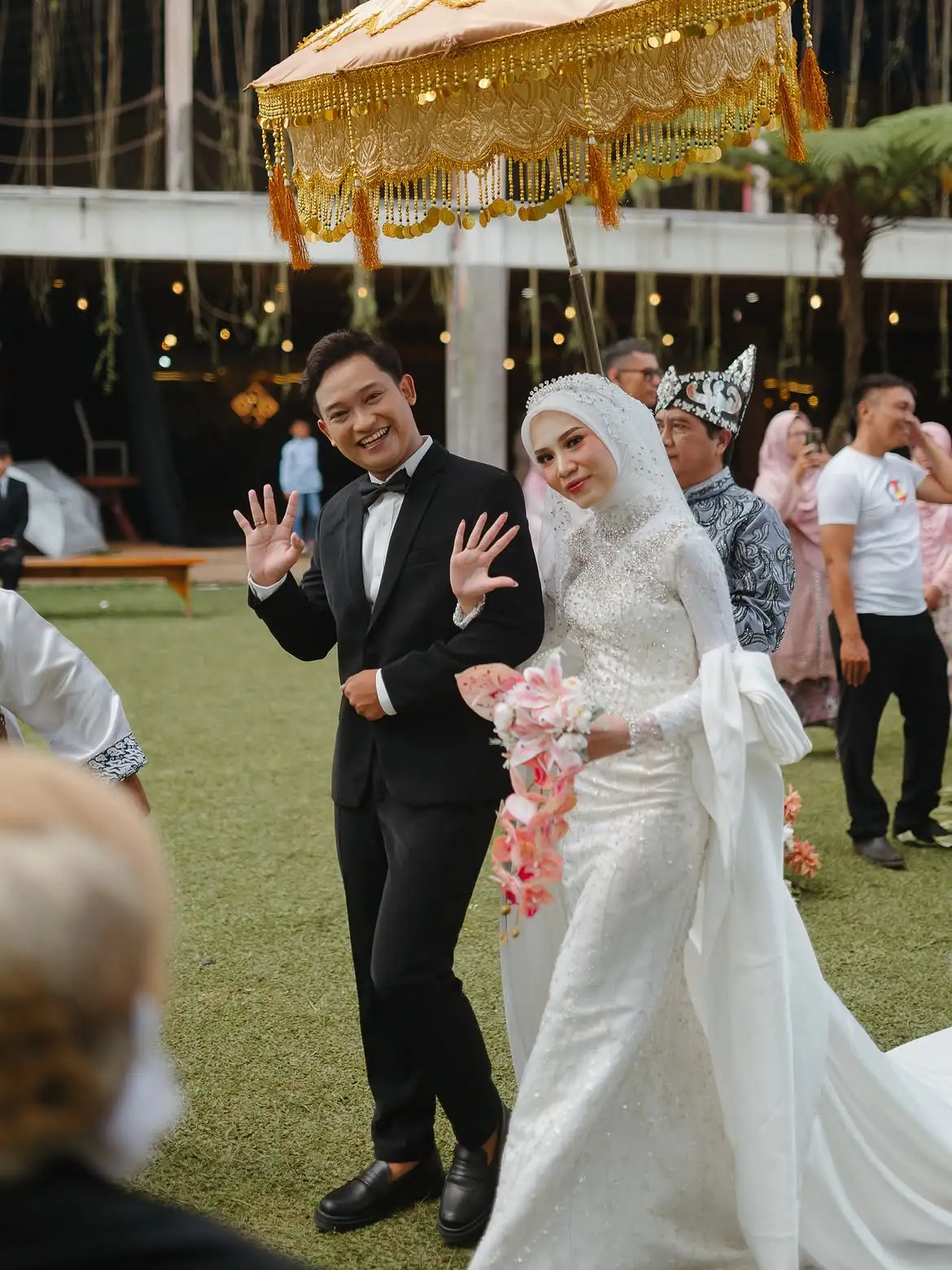 Pengantin berjalan masuk di bawah payung kehormatan emas disaksikan para tamu