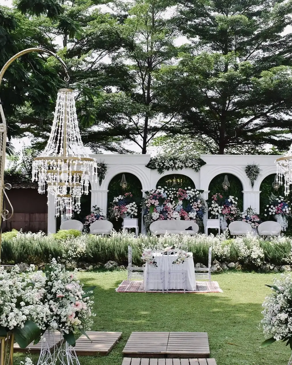 Dekorasi wedding dengan lampu kristal dan gerbang putih di atas rumput